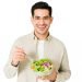 I have a healthy diet. Happy man smiling and eating a bowl of green salad while looking at the camera