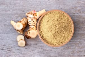 Alpinia galanga powder in wooden bowl and fresh galangal rhizome isolated on wooden table background. Top view.