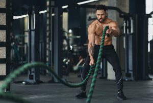 Athletic young man with battle rope doing exercise