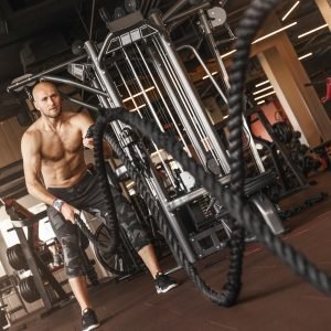 Handsome caucasian muscular man doing battle rope exercise while working out in gym