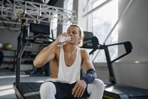 Happy smiling athletic man drinking water taking break after workout in gym