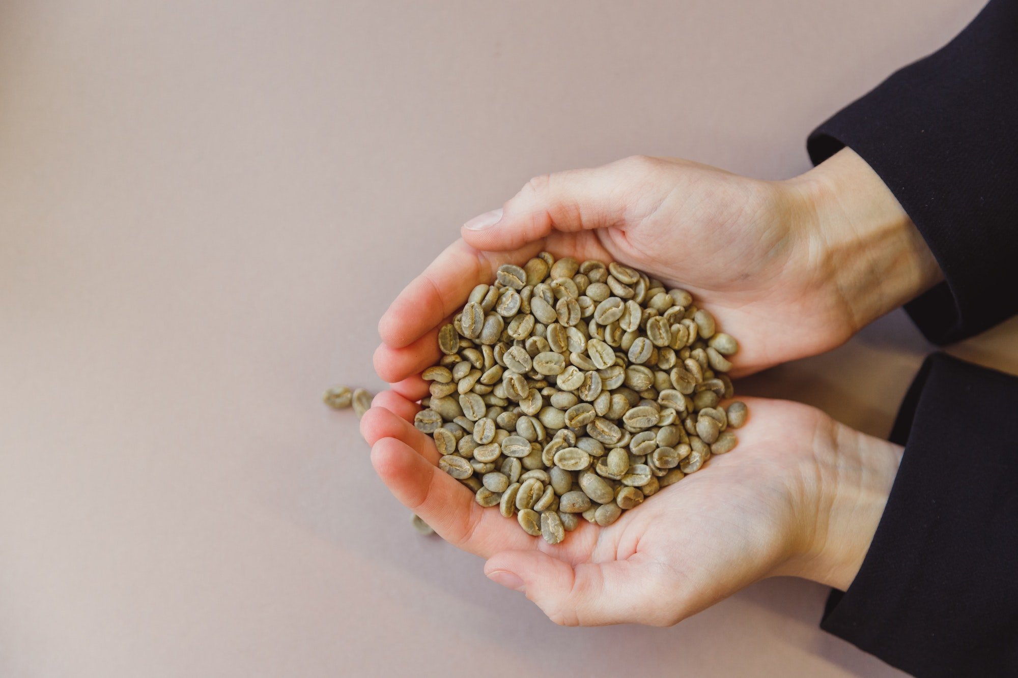 Green coffee beans in woman's hands.