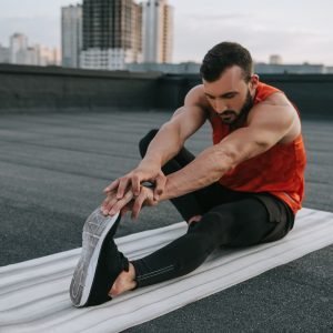 handsome sportsman stretching on yoga mat on roof