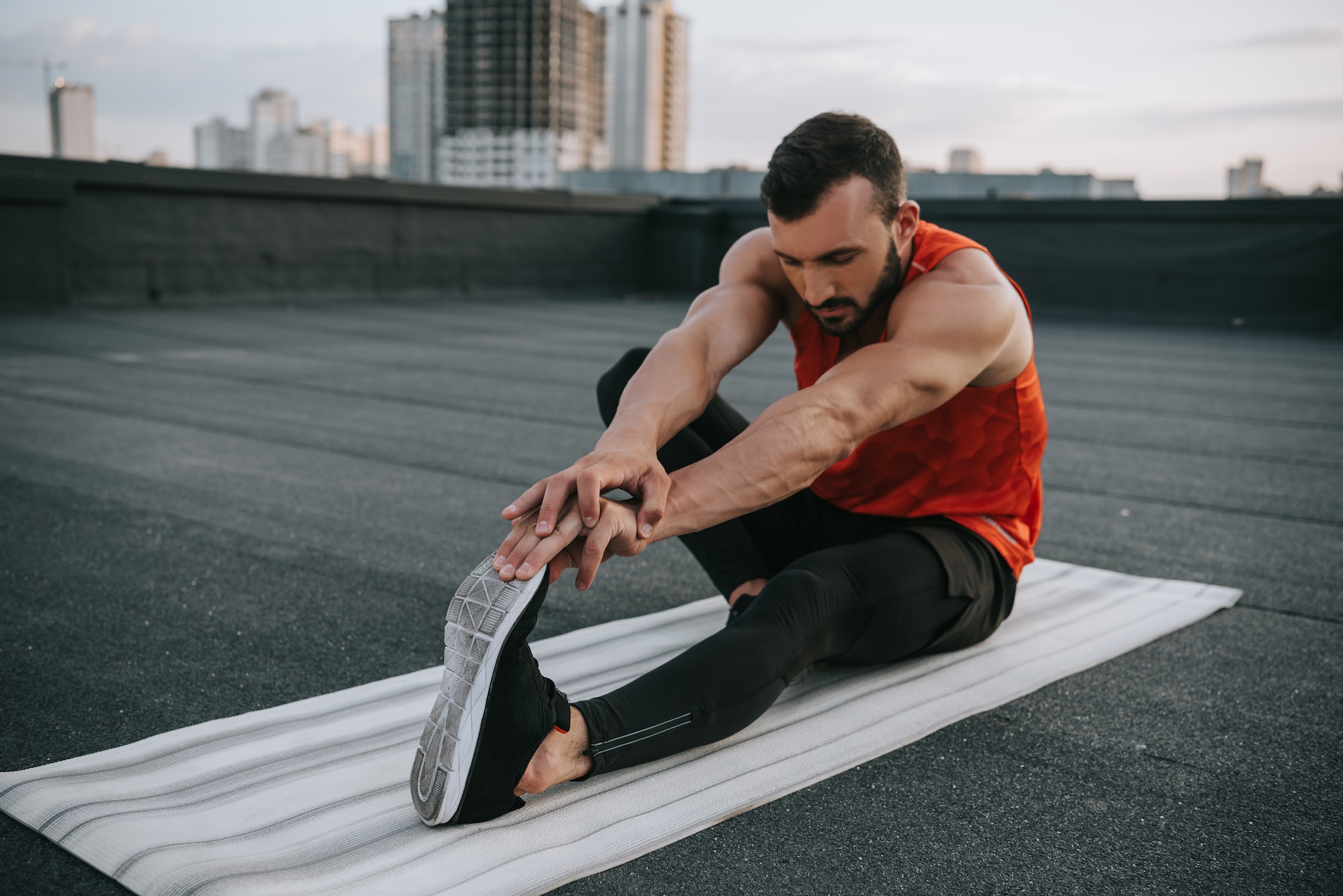 handsome sportsman stretching on yoga mat on roof