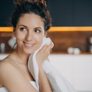 Smiling hispanic girl wiping face by towel enjoy fresh glowing skin after skincare treatment at home