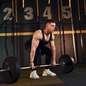 Strong man in sportive clothes lifting barbell in the gym