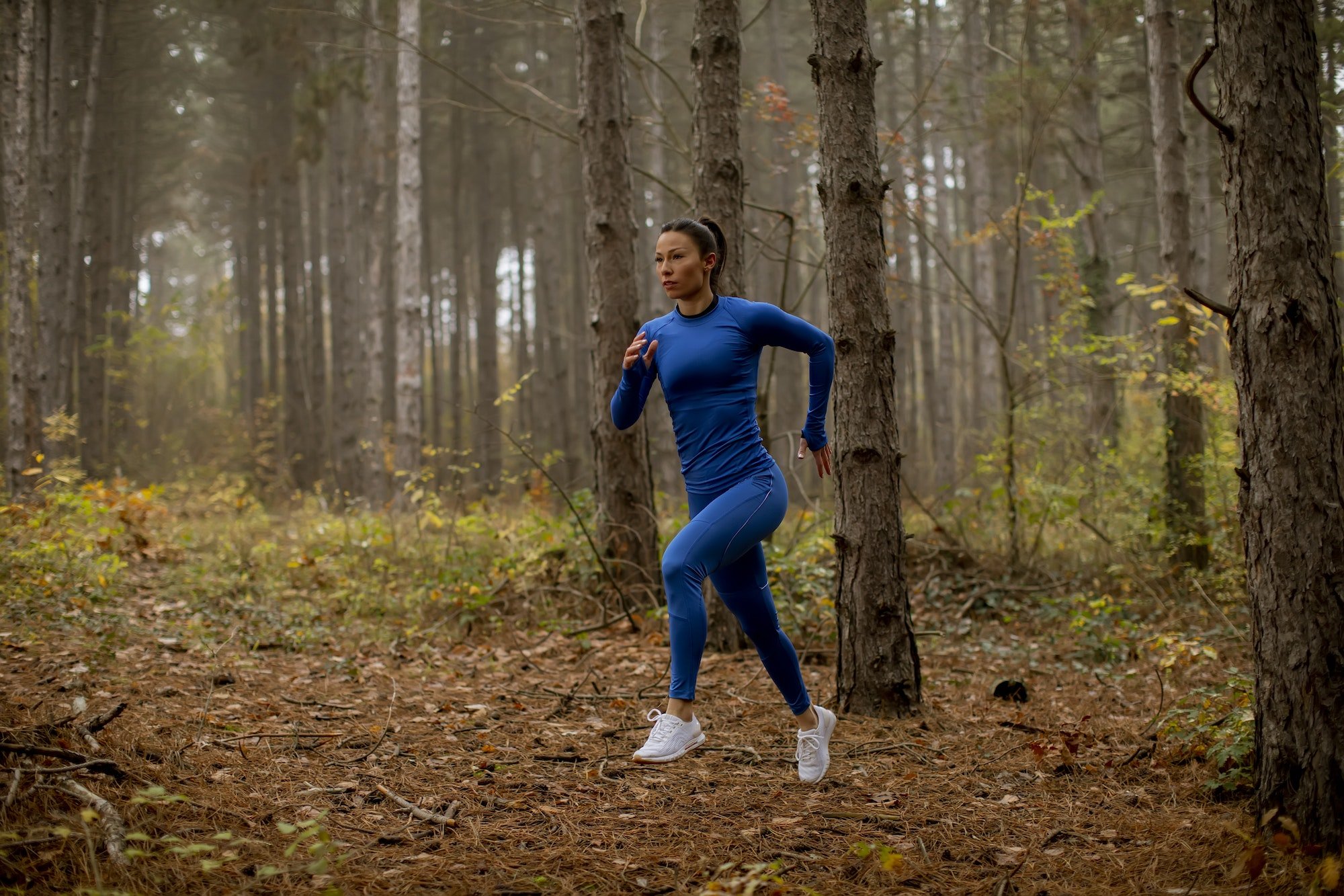 Young woman running on the forest trail at autumn