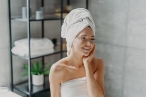 Positive European woman smiles pleasantly, touches healthy skin