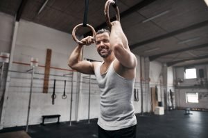 Smiling man resting after exercising on rings at the gym
