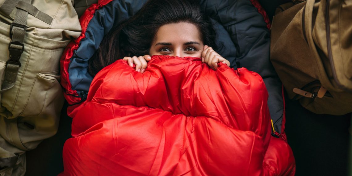 A young woman in a comfortable sleeping bag in a tent, top view. A tourist in a sleeping bag