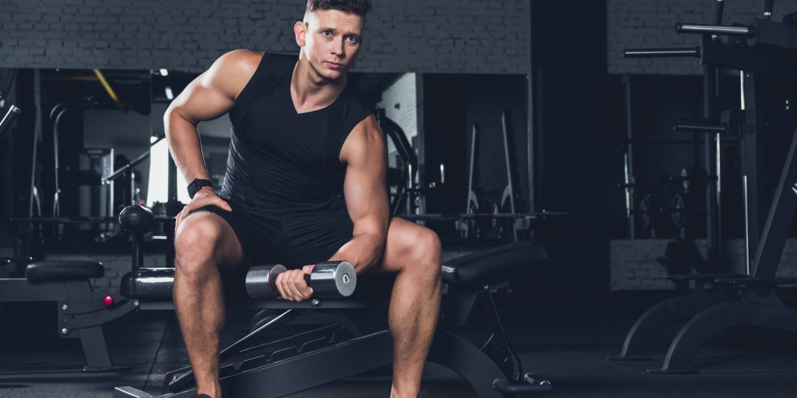 attractive man pumping muscles with dumbbell in hand in gym
