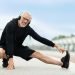 Cheerful healthy elderly man stretching legs in park with music