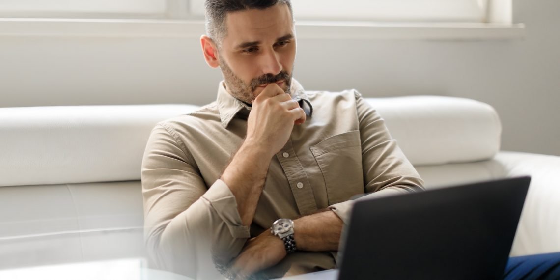 Focused thoughtful businessman using laptop and thinking of project, making decision, looking at