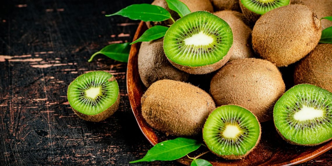 Fresh kiwi with leaves on a wooden plate.