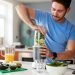 Man Making Healthy Juice Drink With Fresh Ingredients In Electric Juicer After Exercise
