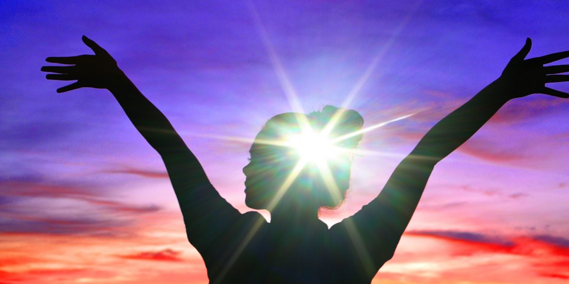 Mental health concept, Girl female holding her hands in the air at sunset with bright light on head.