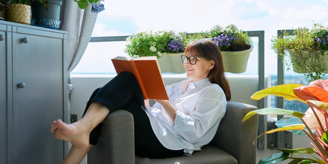 Middle-aged relaxed happy woman reading book, sitting at home