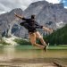 Rear view of man jumping on wooden deck by lake. Happy person in idyllic place in nature.