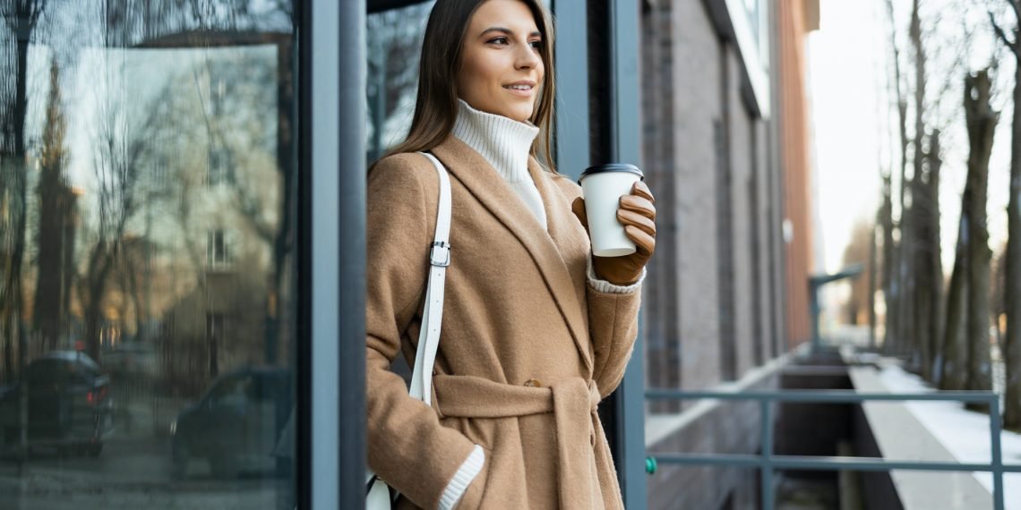 Young brunette in a brown coat with a cup of coffee in her hand
