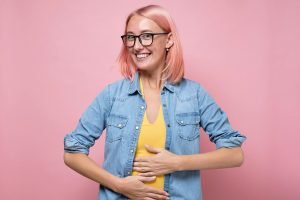 Happy caucasian woman having no problems with digestion holding hands on belly.