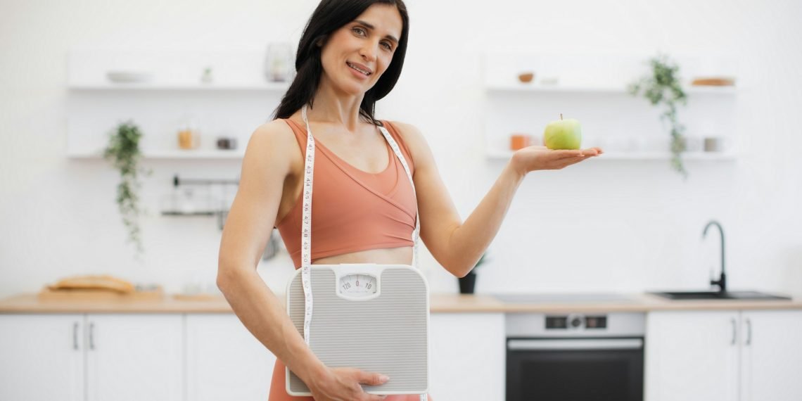 Health coach with measuring tape, scales and apple at home