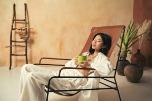 Asian girl relaxing on lounger with mug of tea, meditating, spending weekend on spa resort