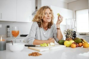 Fruits are natures candy. Shot of a woman preparing and eating fruit before making a smoothie.