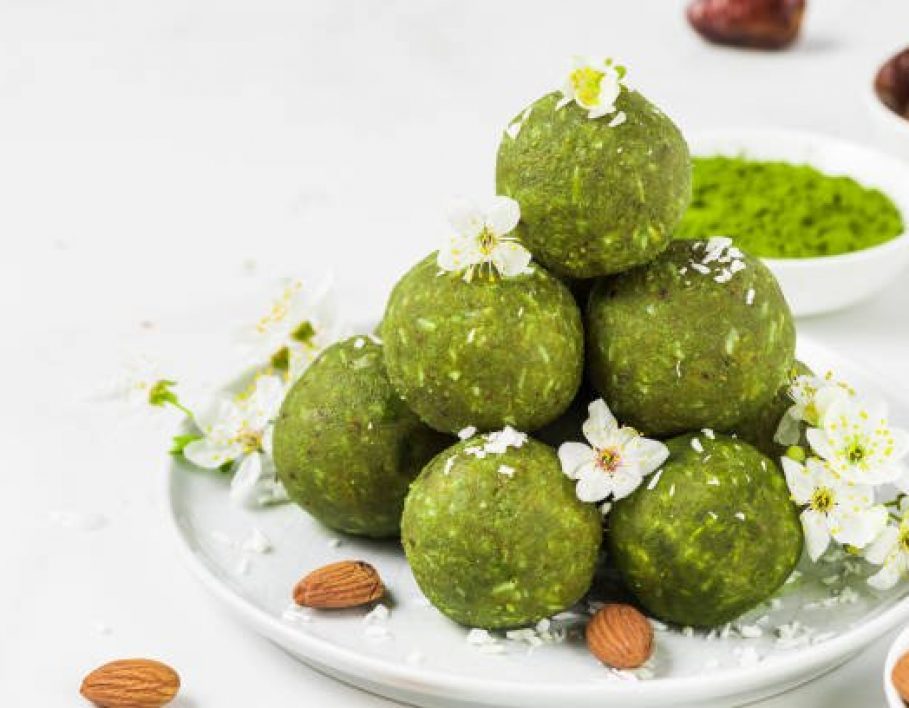 Green matcha energy balls or energy bites made of dates and nuts with spring flowers. Healthy vegan diet snacks. Food styling. close up with copy space
