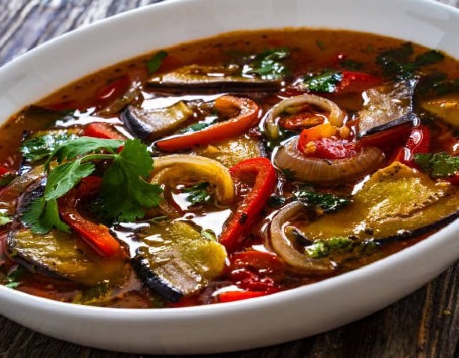 Vegetable soup - fried eggplant, red bell pepper,cilantro, tomato and onion on wooden table
