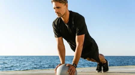 athletic adult man doing push ups with fit ball on seashore