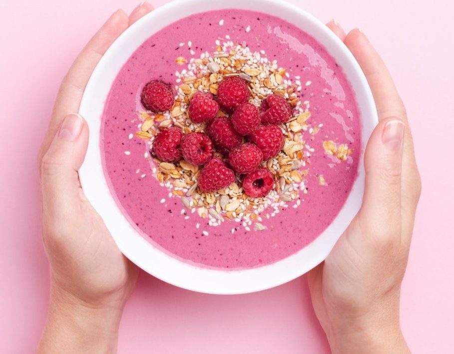 Female`s Hands Holding Raspberries Smothie Bowl on Pink Background.