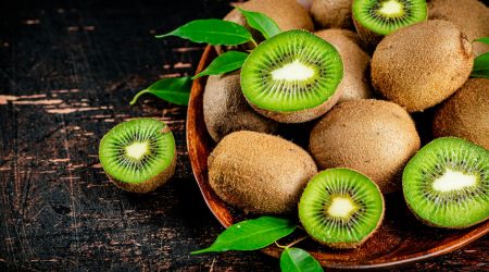 Fresh kiwi with leaves on a wooden plate.