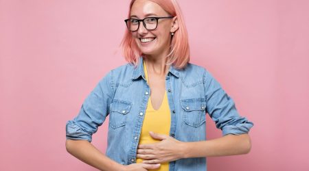 Happy caucasian woman having no problems with digestion holding hands on belly.
