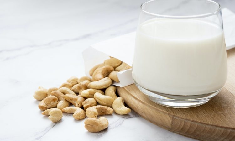 Plant based milk with heap of cashew nuts on wooden board.