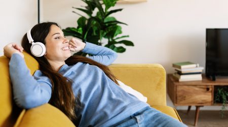 Relaxed smiling young adult woman with headphones sitting on sofa at home