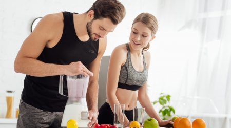 sportive man preparing smoothie near happy girl and fruits