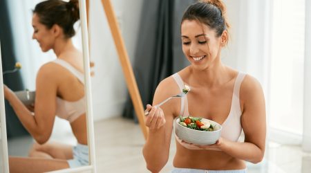 Young happy woman enjoying while eating healthy salad at home.