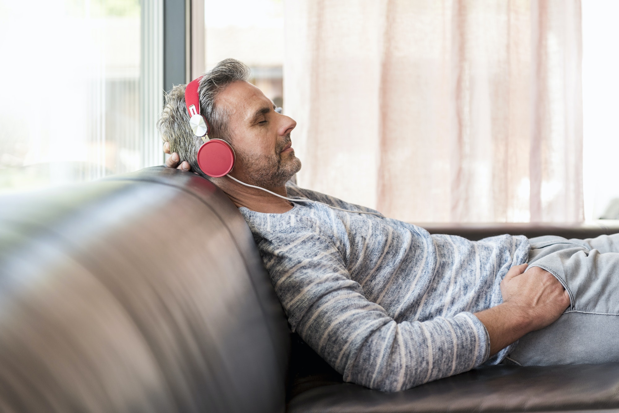 Relaxed mature man lying on couch at home wearing headphones