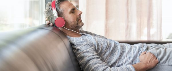 Relaxed mature man lying on couch at home wearing headphones
